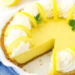 A lemonade icebox pie with one slice missing and two fresh lemons behind it