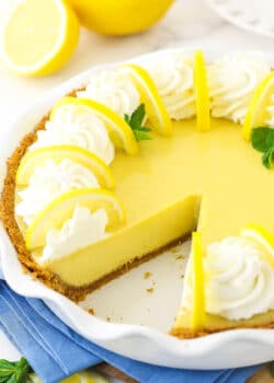 A lemonade icebox pie with one slice missing and two fresh lemons behind it