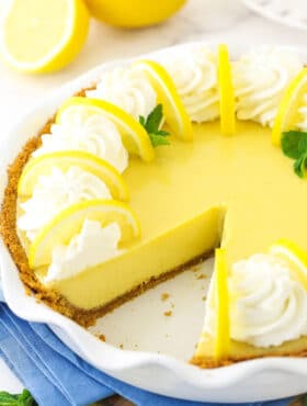 A lemonade icebox pie with one slice missing and two fresh lemons behind it