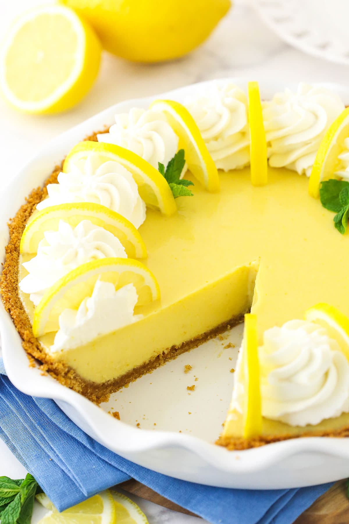 A lemonade icebox pie with one slice missing and two fresh lemons behind it