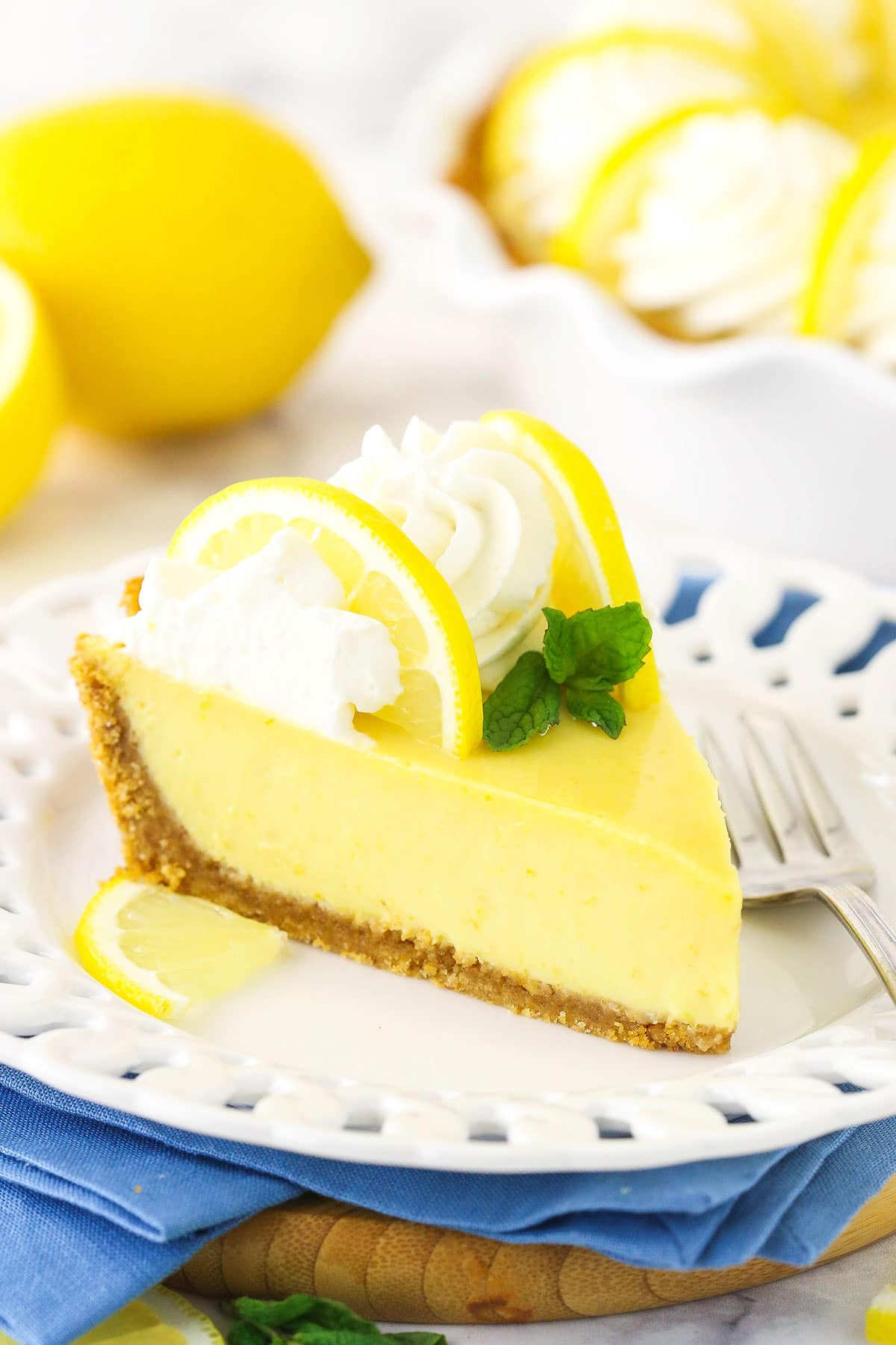 A slice of lemonade icebox pie on a marble countertop with the remaining pie in the background