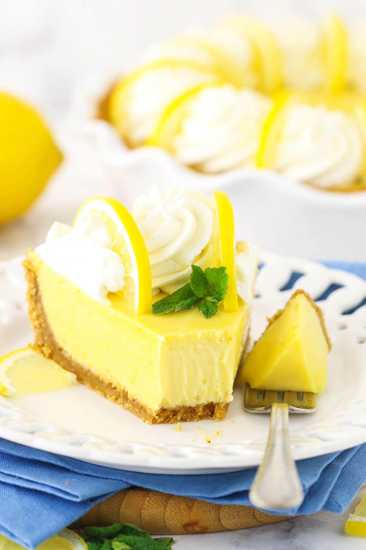 A piece of lemon pie on a fancy dessert plate with one bite on a fork beside the slice