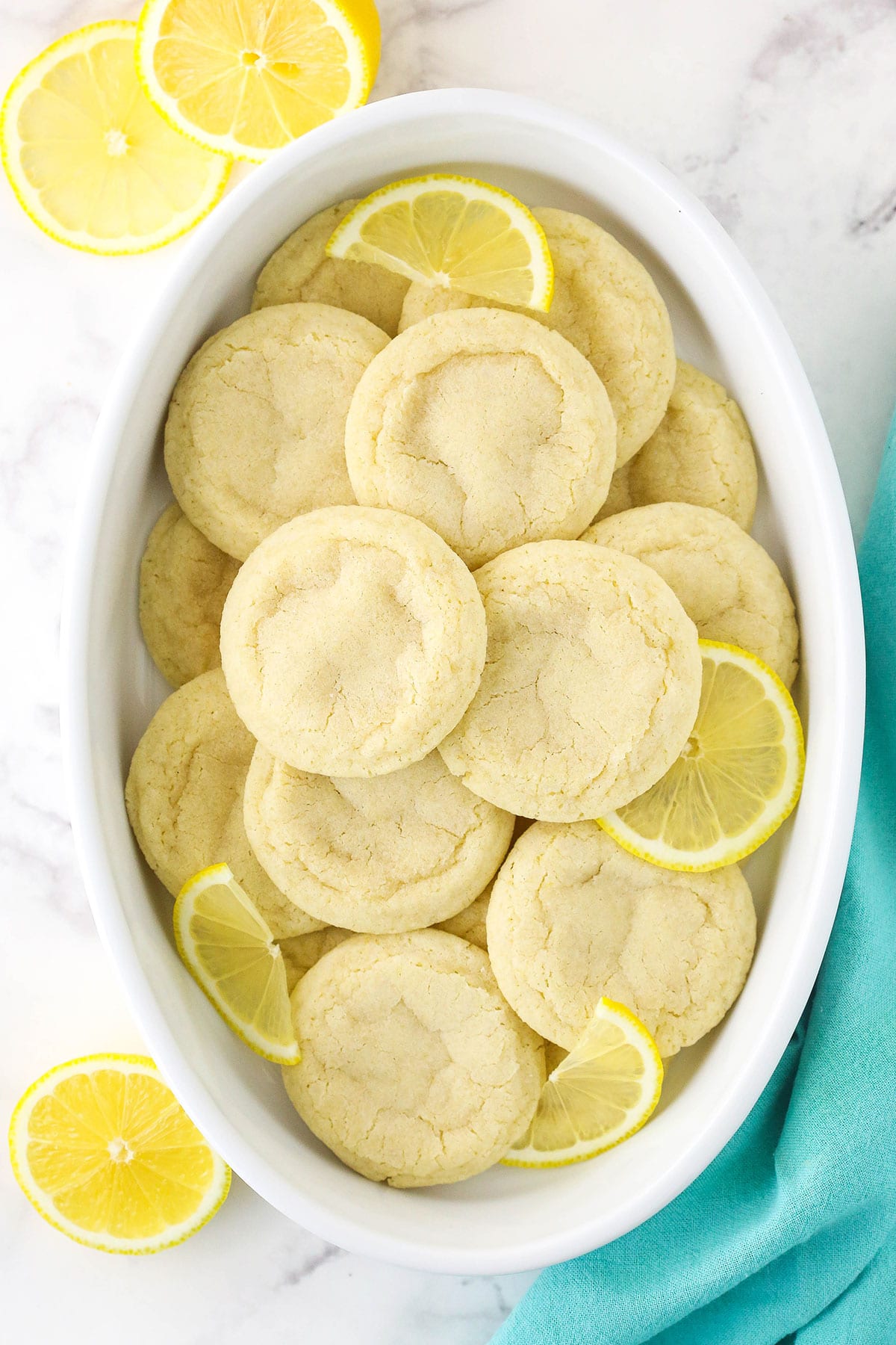 An overhead shot of a bunch of sugar cookies inside of a bowl beside a teal napkin