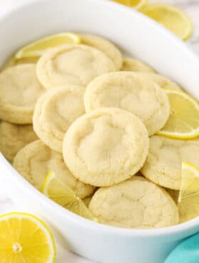 A Tupperware tub filled with lemon sugar cookies and a few fresh lemon slices