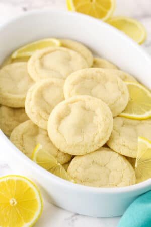 A Tupperware tub filled with lemon sugar cookies and a few fresh lemon slices