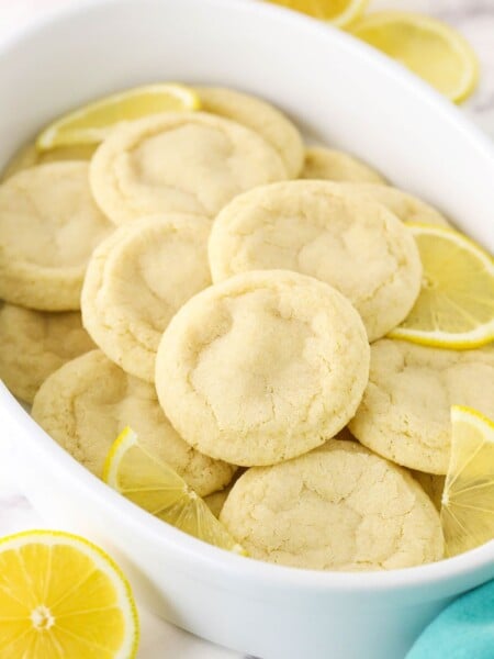 A Tupperware tub filled with lemon sugar cookies and a few fresh lemon slices