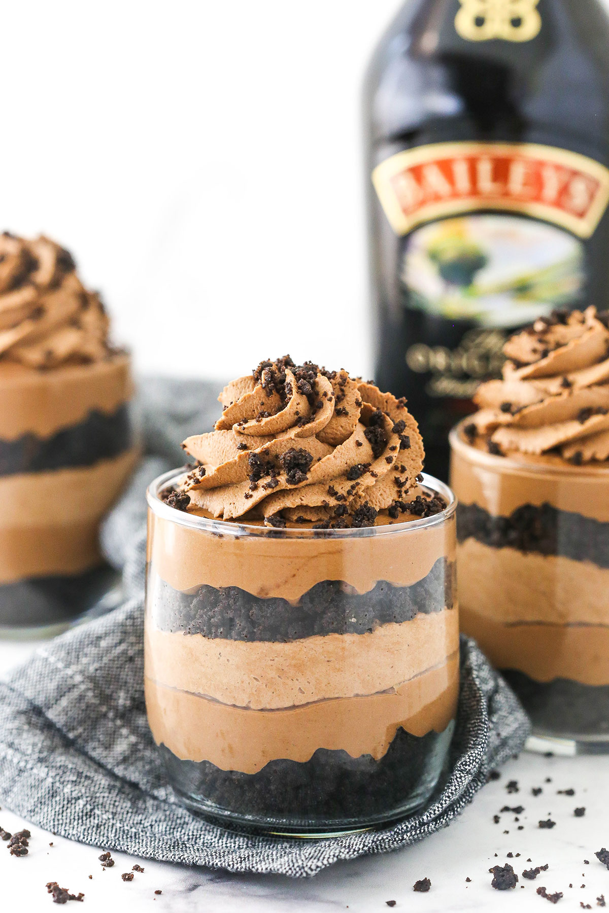 Three no-bake Baileys cheesecakes on top of a marble countertop beside a kitchen towel