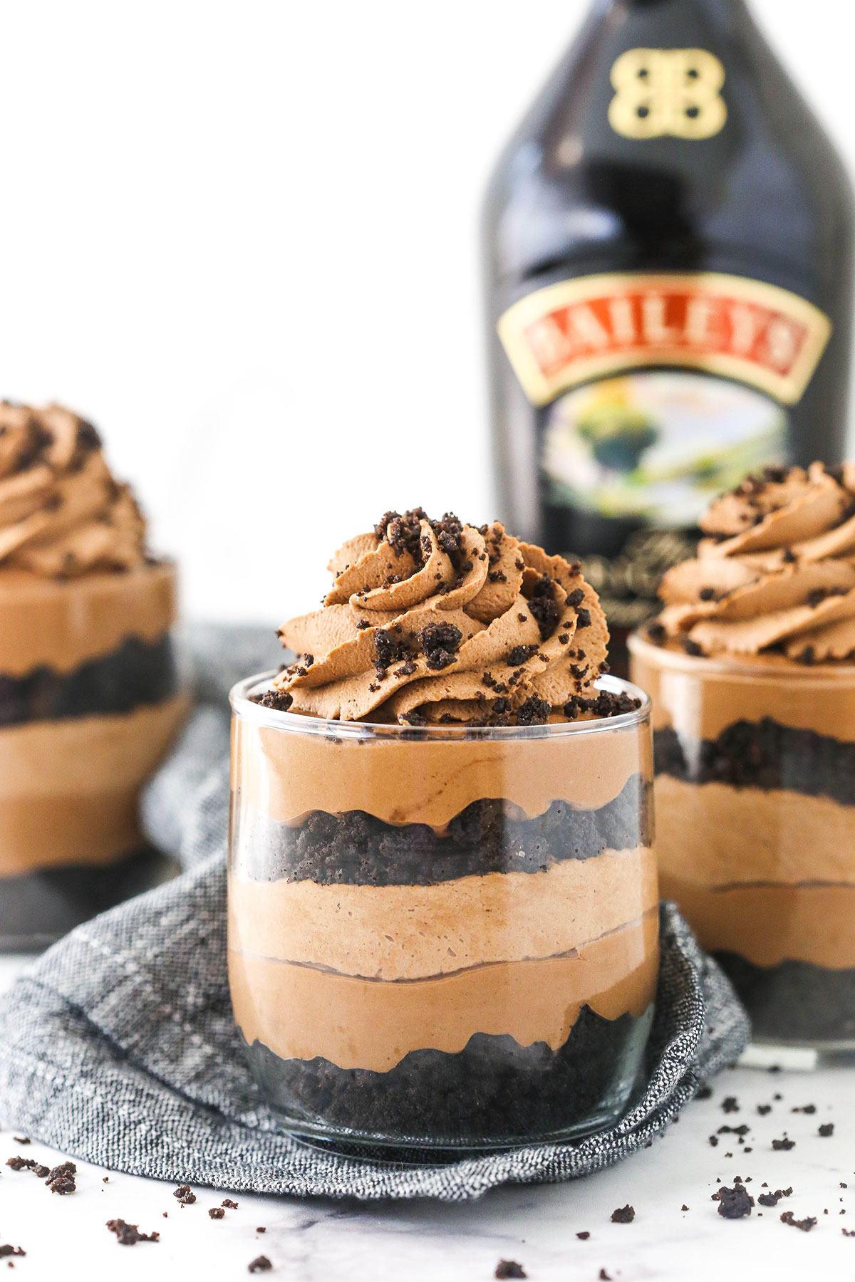 A Baileys cheesecake trifle on a countertop beside two more trifles and a bottle of Baileys