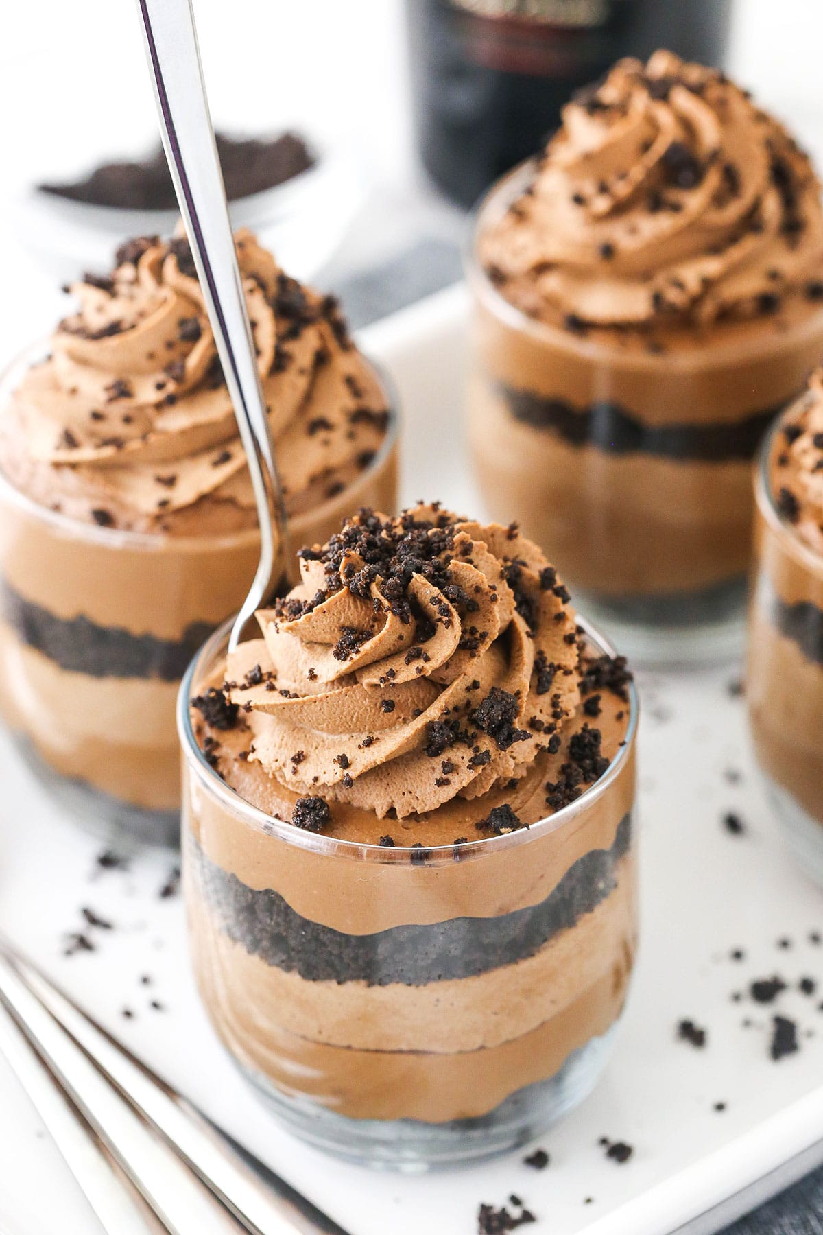 Four Baileys cheesecake trifles on a serving platter with a spoon stuck into the one in front