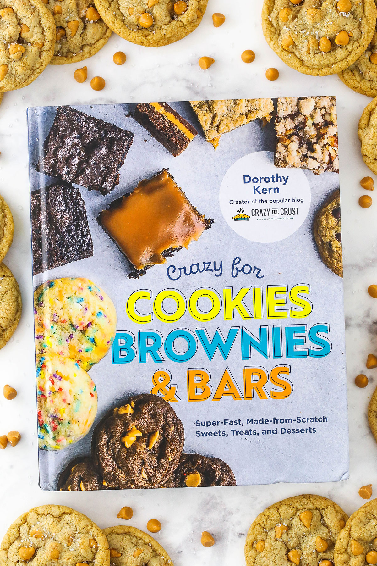 Overhead view of a Crazy for Cookies, Brownies and Bars cookbook surrounded by salted butterscotch cookies on a white surface.