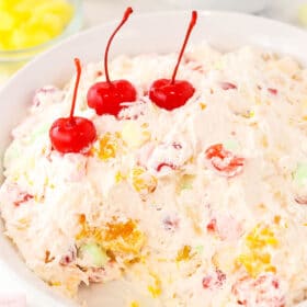 A serving platter filled with Cool Whip fruit salad with three maraschino cherries placed on top