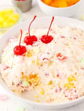 A serving platter filled with Cool Whip fruit salad with three maraschino cherries placed on top