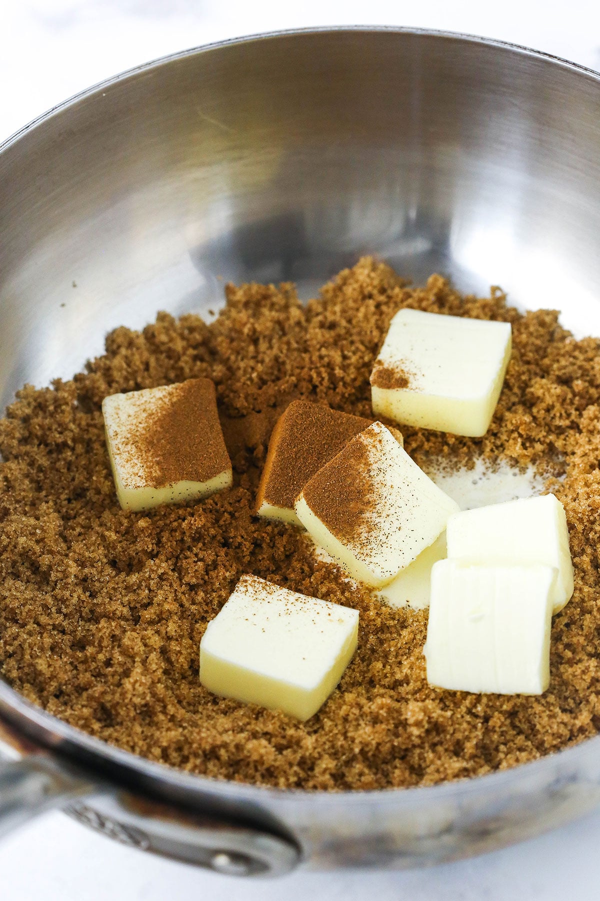 Brown sugar inside of a metal saucepan with seven squares of salted butter