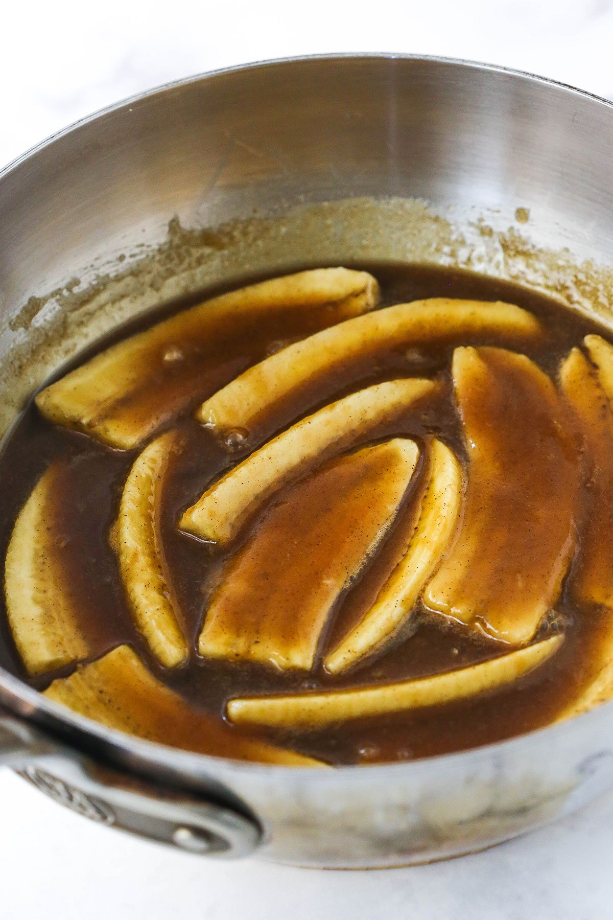 Bananas foster sitting inside of a large metal skillet on a kitchen countertop