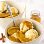 Extra bananas foster sauce being drizzled over a dessert bowl filled with bananas foster and vanilla ice cream