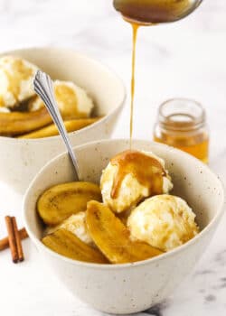 Extra bananas foster sauce being drizzled over a dessert bowl filled with bananas foster and vanilla ice cream