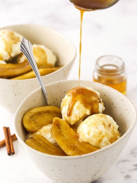 Extra bananas foster sauce being drizzled over a dessert bowl filled with bananas foster and vanilla ice cream