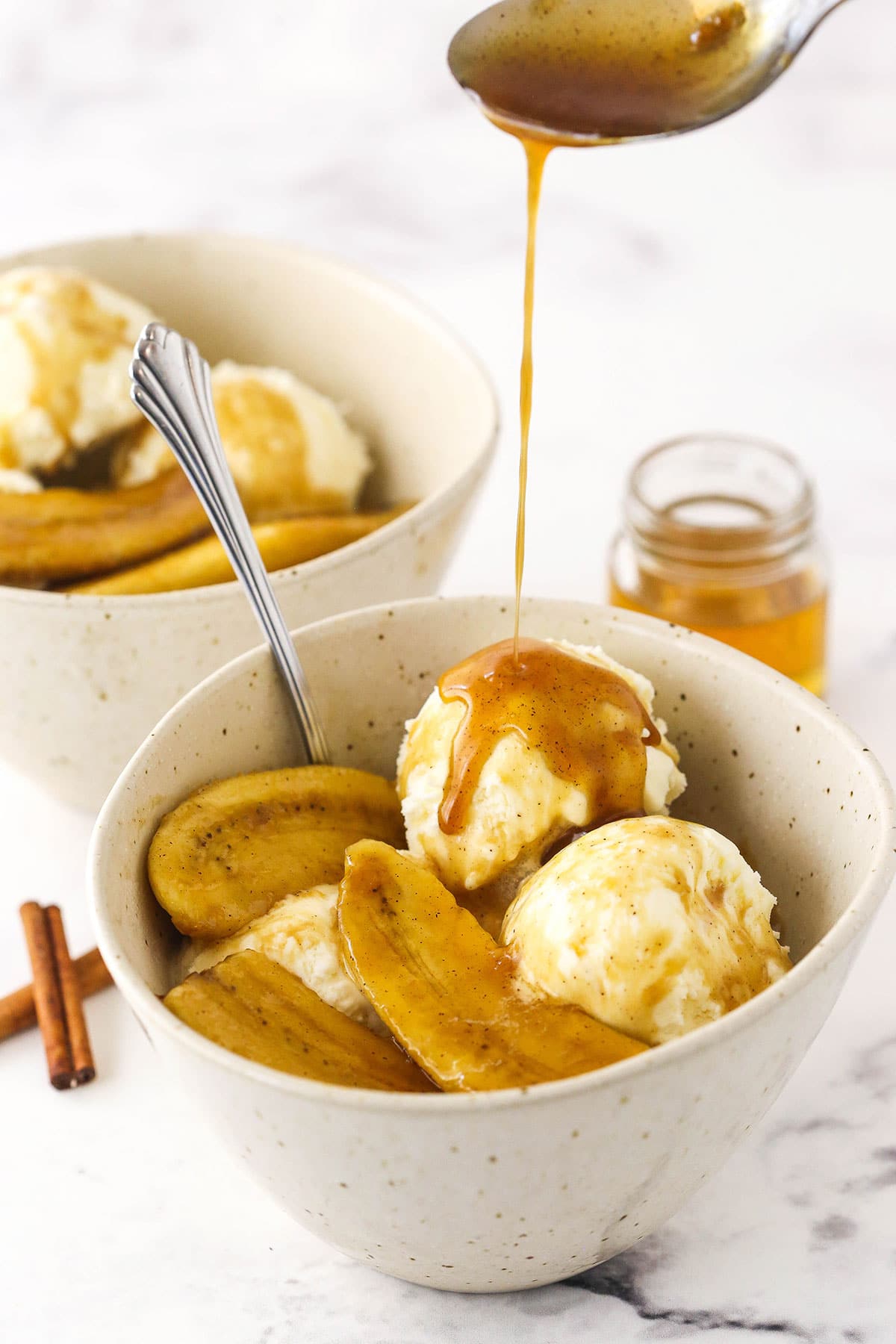 Extra bananas foster sauce being drizzled over a dessert bowl filled with bananas foster and vanilla ice cream