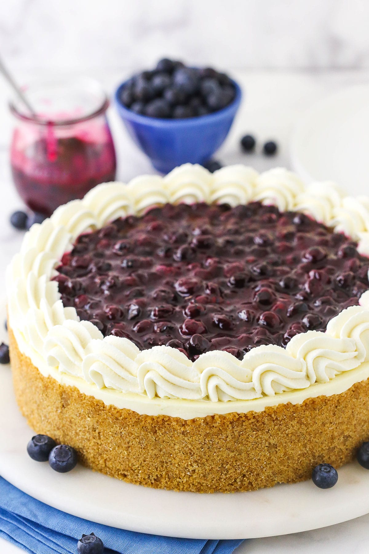A no-bake blueberry cheesecake on top of a serving plate with a stack of blue napkins underneath the plate