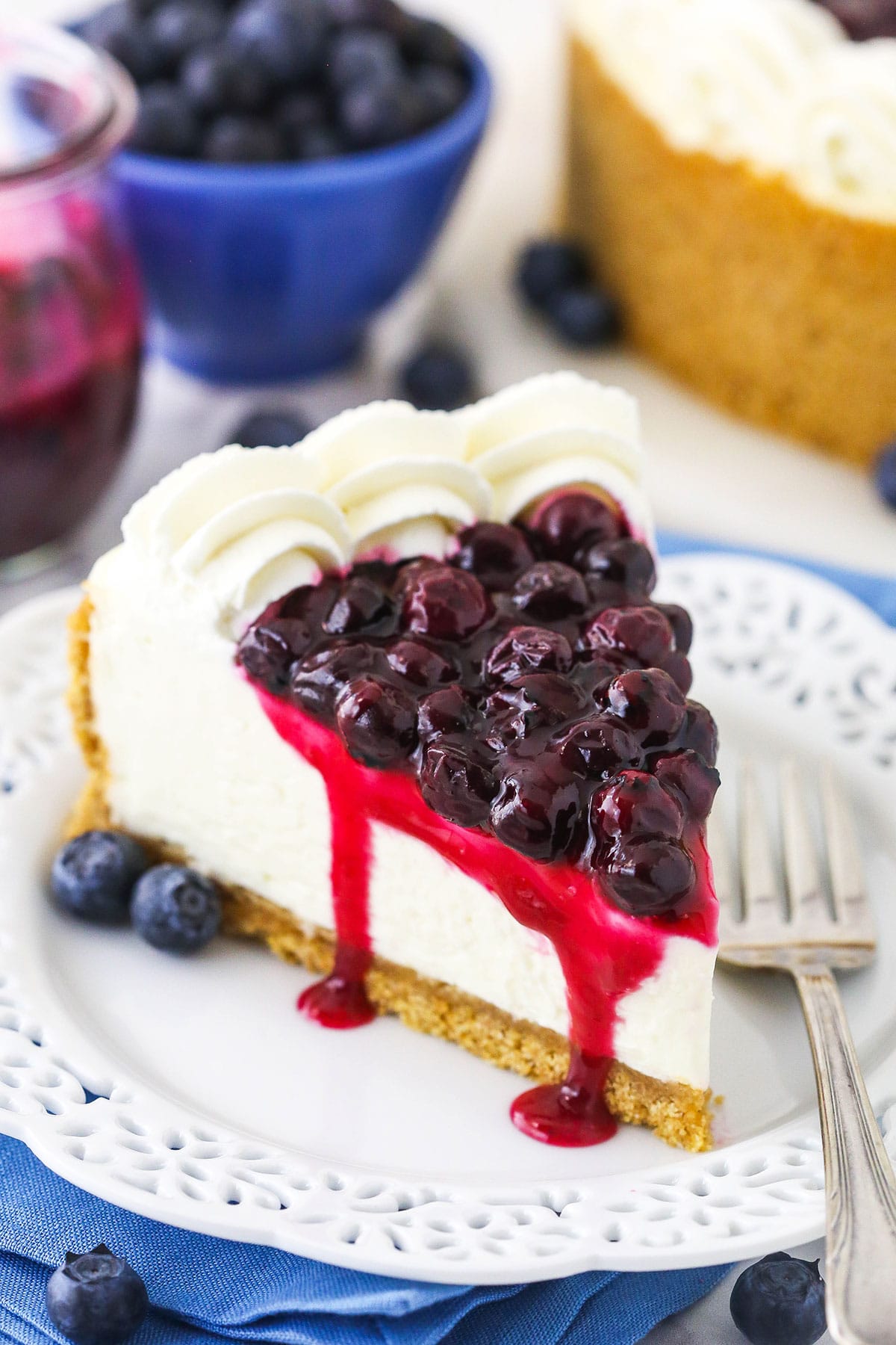 A close-up shot of a slice of no-bake cheesecake topped with homemade blueberry sauce and whipped cream