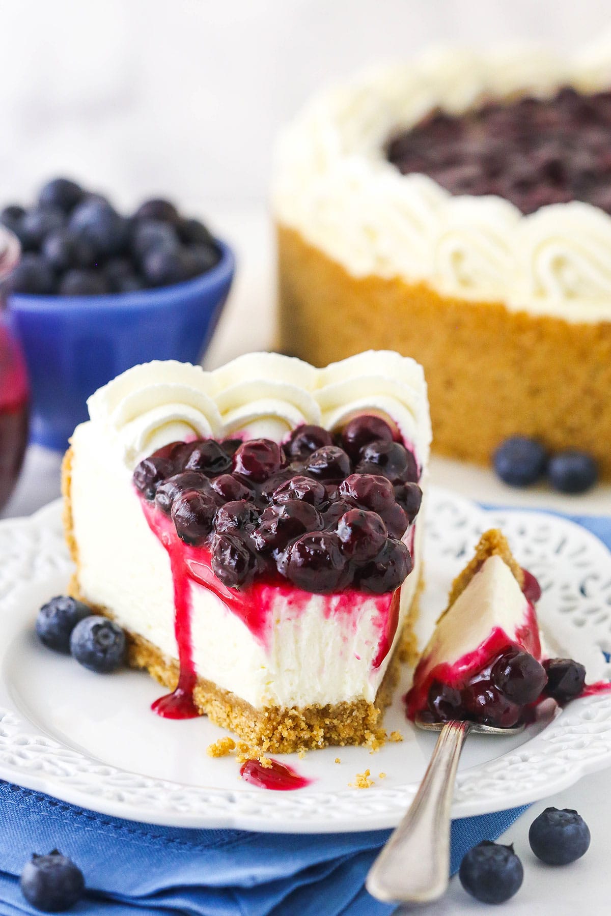 A slice of no-bake blueberry cheesecake on a plate with one bite on a fork