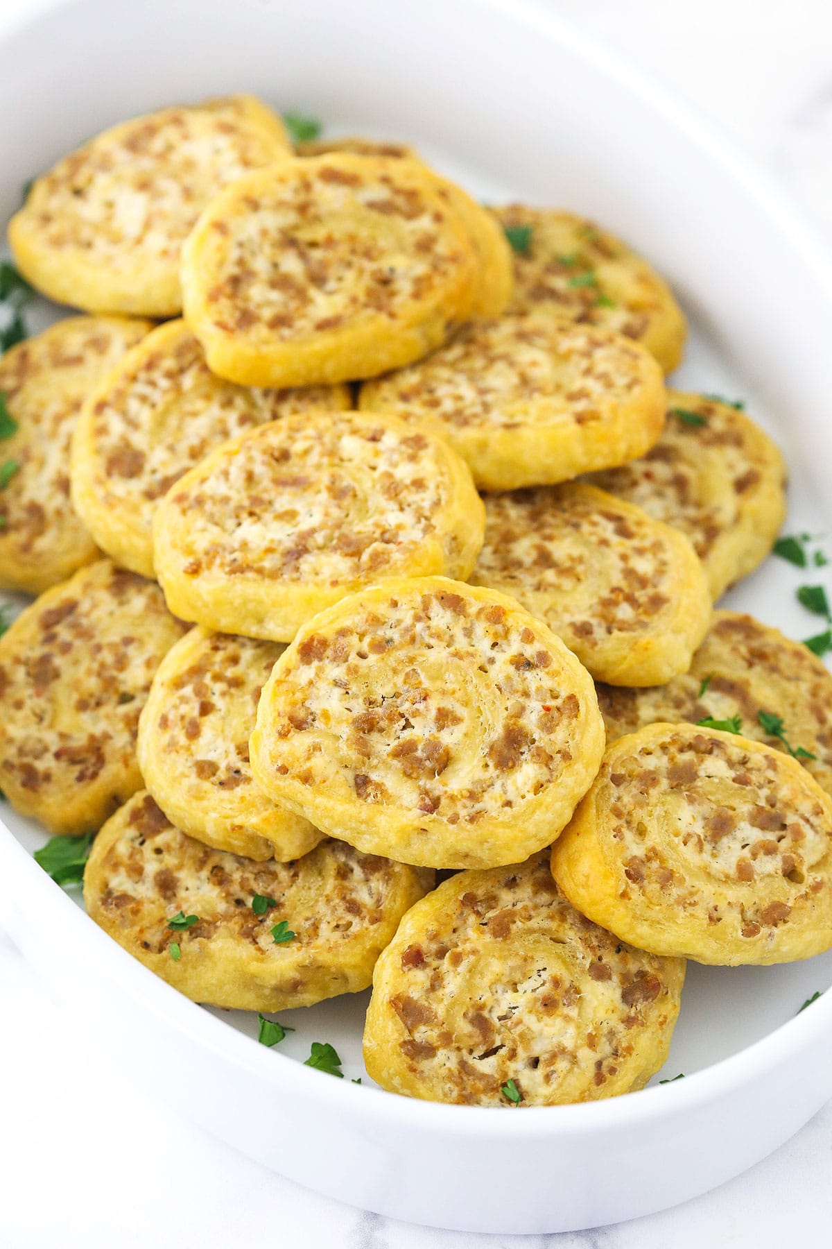 Sausage pinwheels garnished with freshly chopped herbs on top of a kitchen counter