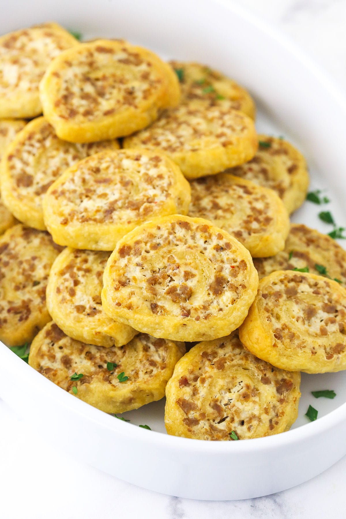 Savory sausage pinwheels inside of a large serving dish on top of a marble surface