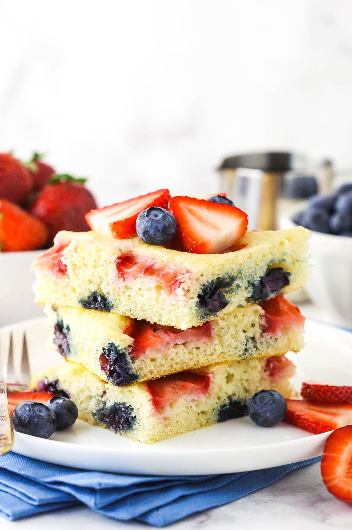 A stack of three sheet pan pancakes on a plate with fresh blueberries and strawberries