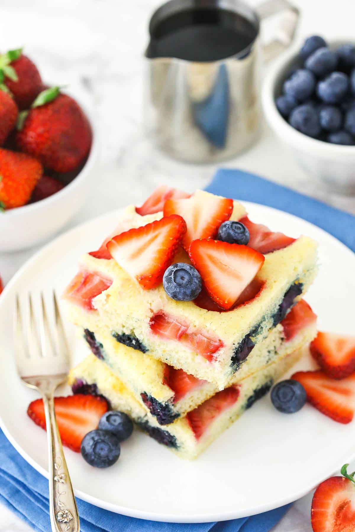 Three oven-baked pancakes piled on top of a white plate with two bowls of berries behind them