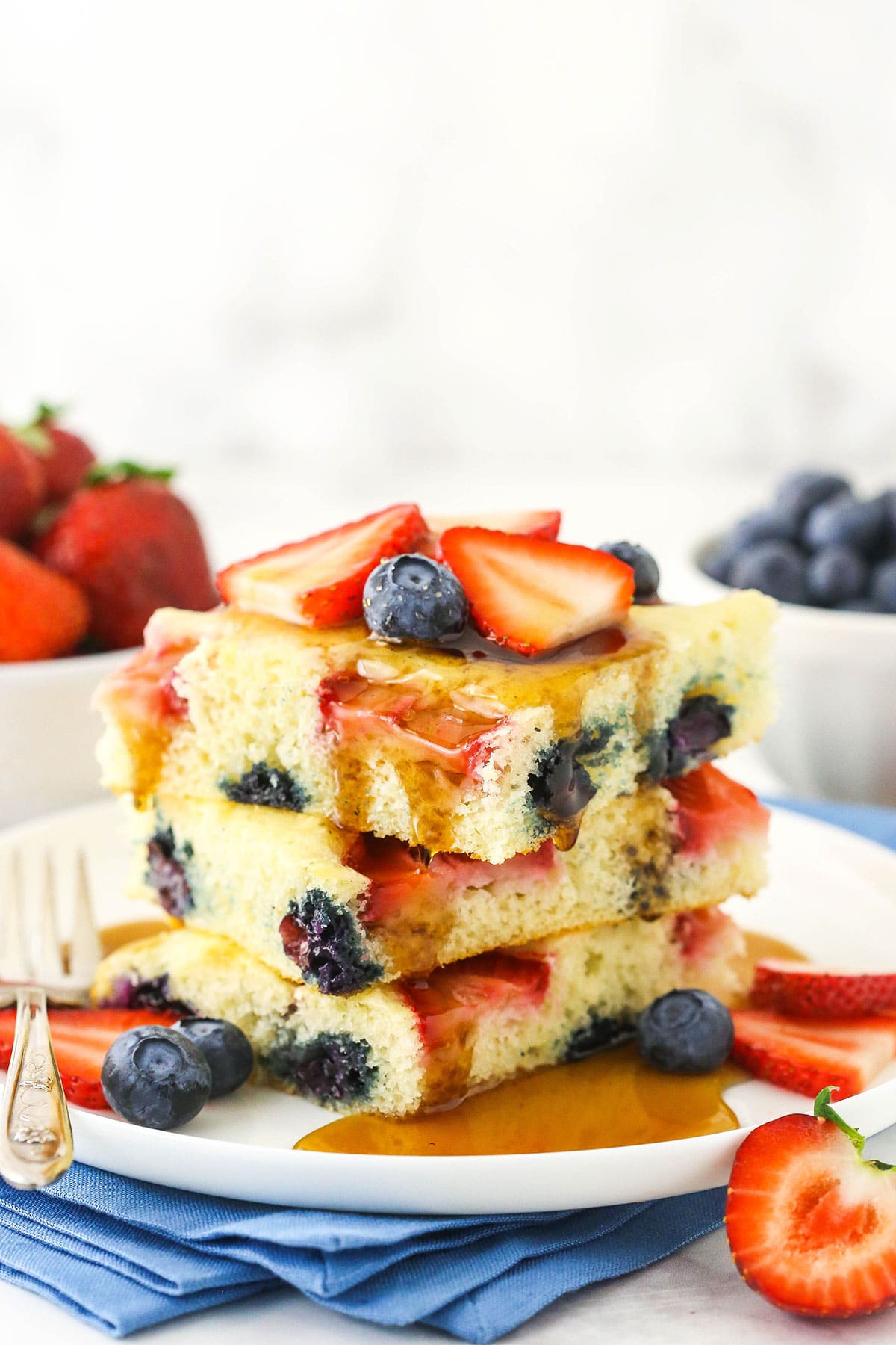 Three sheet pan pancakes stacked on top of one another with fresh fruit and maple syrup on top