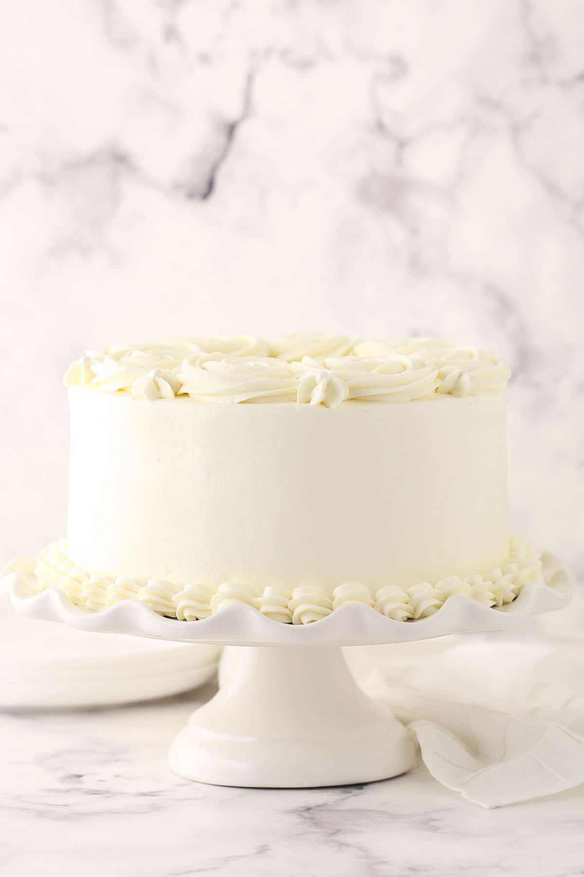 A white cake on a dessert stand with whipped buttercream frosting spread onto it smoothly