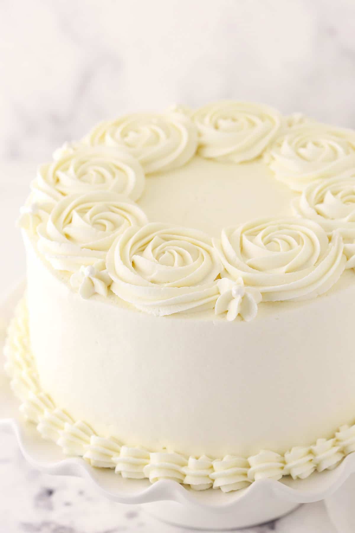 A frosted white cake with rosette designs piped around the top rim