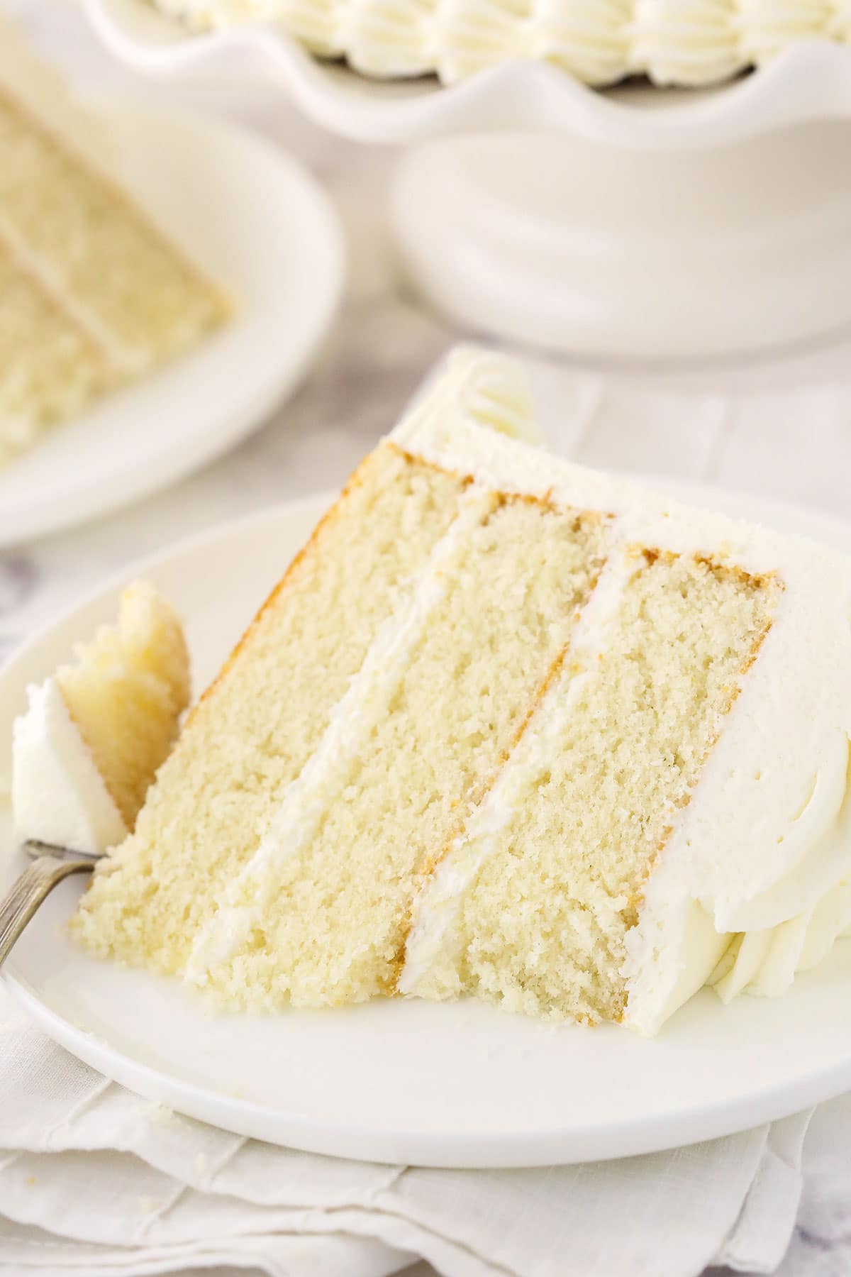 A slice of white cake on a plate with one bite on a metal fork