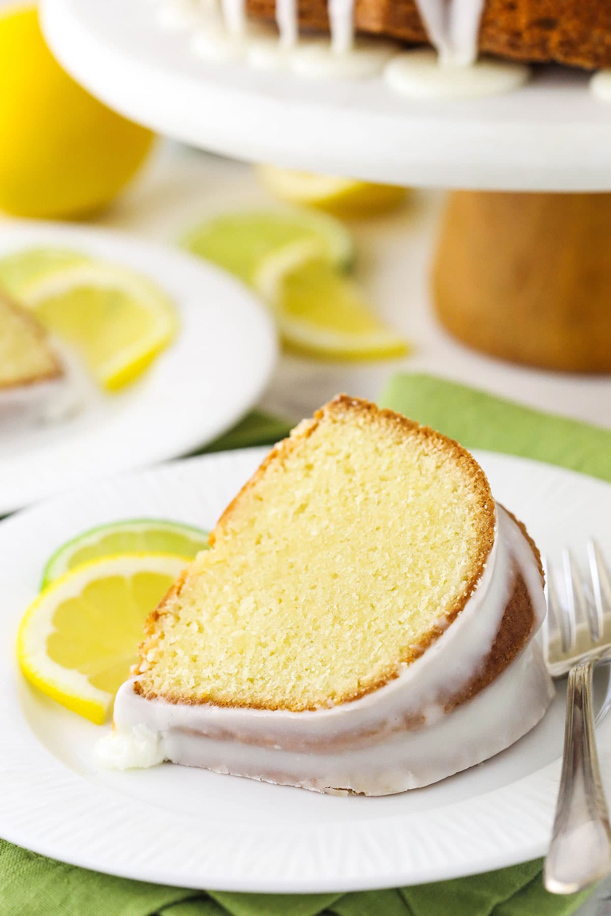 A slice of 7UP pound cake on a plate with a slice of lemon, a slice of lime and a fork