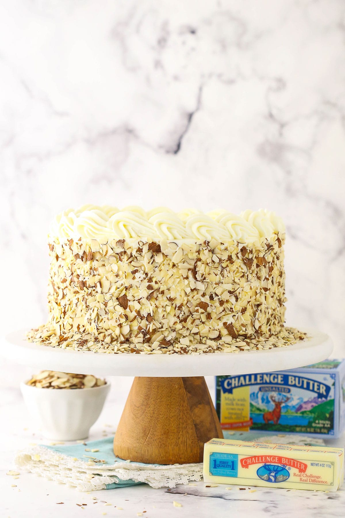 cake with sliced almonds on sides on marble cake stand with challenge butter next to it