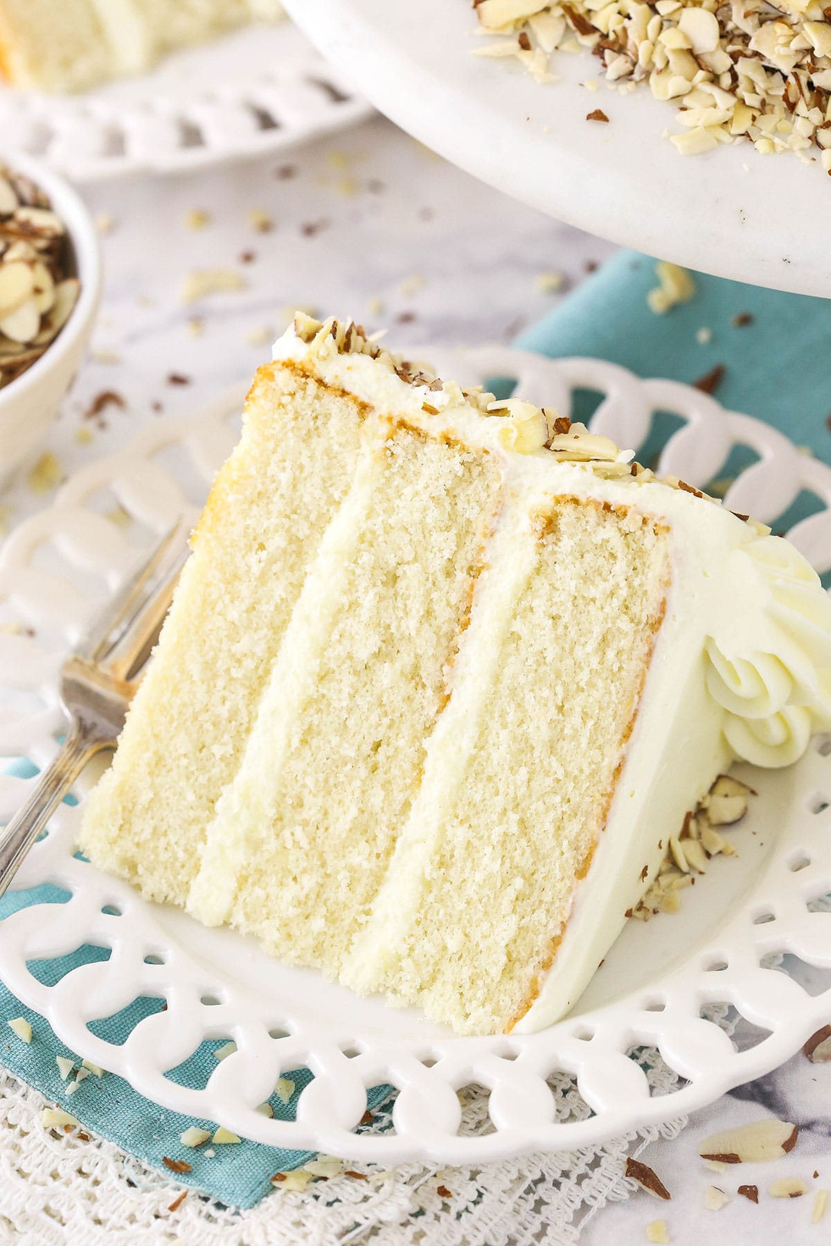 slice of almond cream cake on white plate and blue napkin