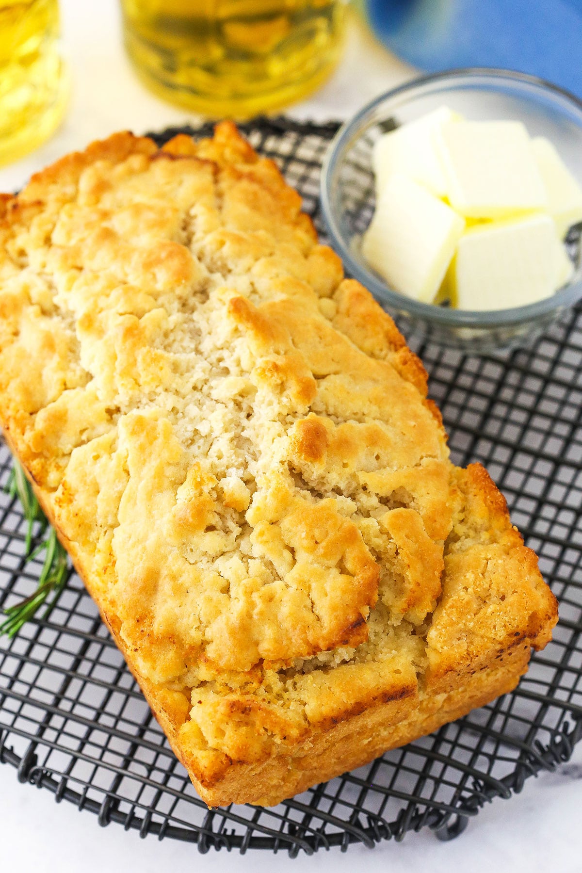 A loaf of homemade quick bread on a circular cooling rack with butter in a bowl beside it