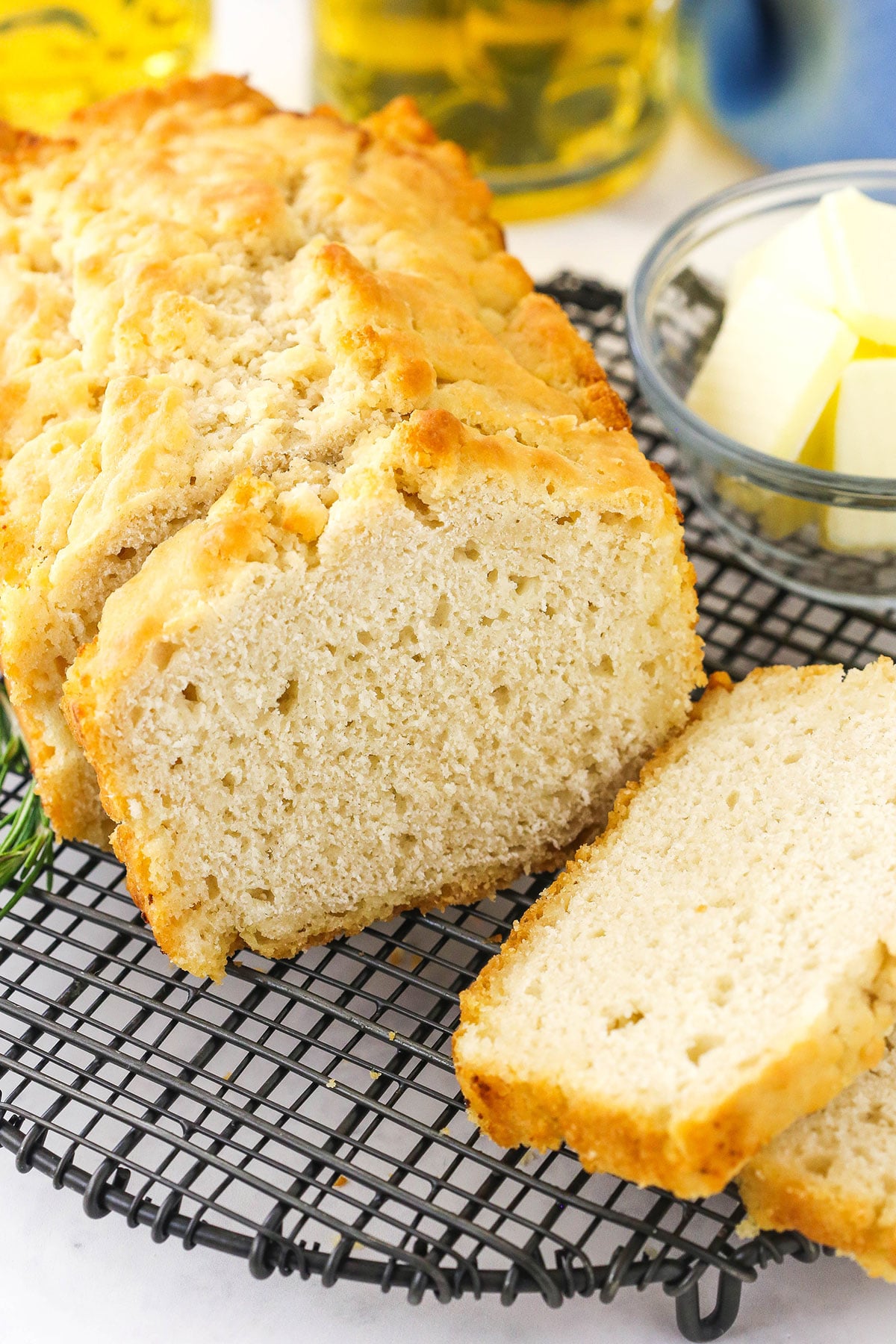 Homemade beer bread on a wire rack with a bowl of butter and a glass of beer in the background