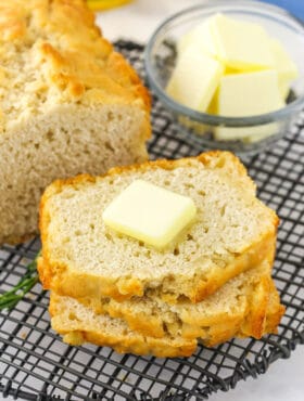 A slice of beer bread on a cooling rack with a pat of butter on top