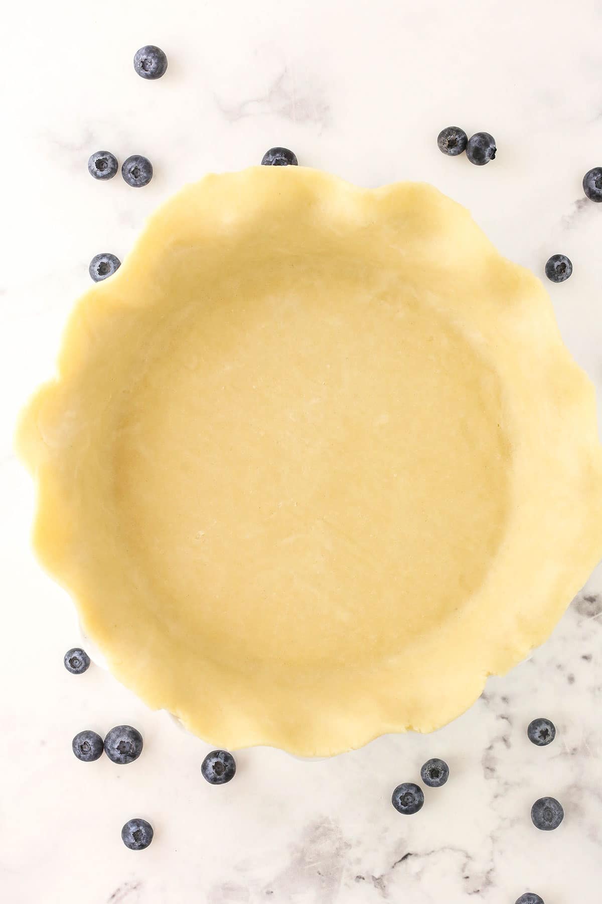 A pie crust pressed into a pan on top of a marble counter