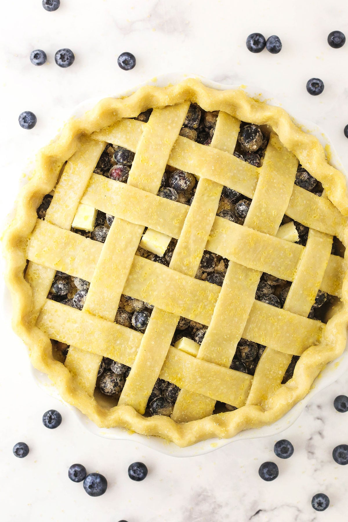 An unbaked blueberry pie brushed with eggwash and sprinkled with turbinado sugar