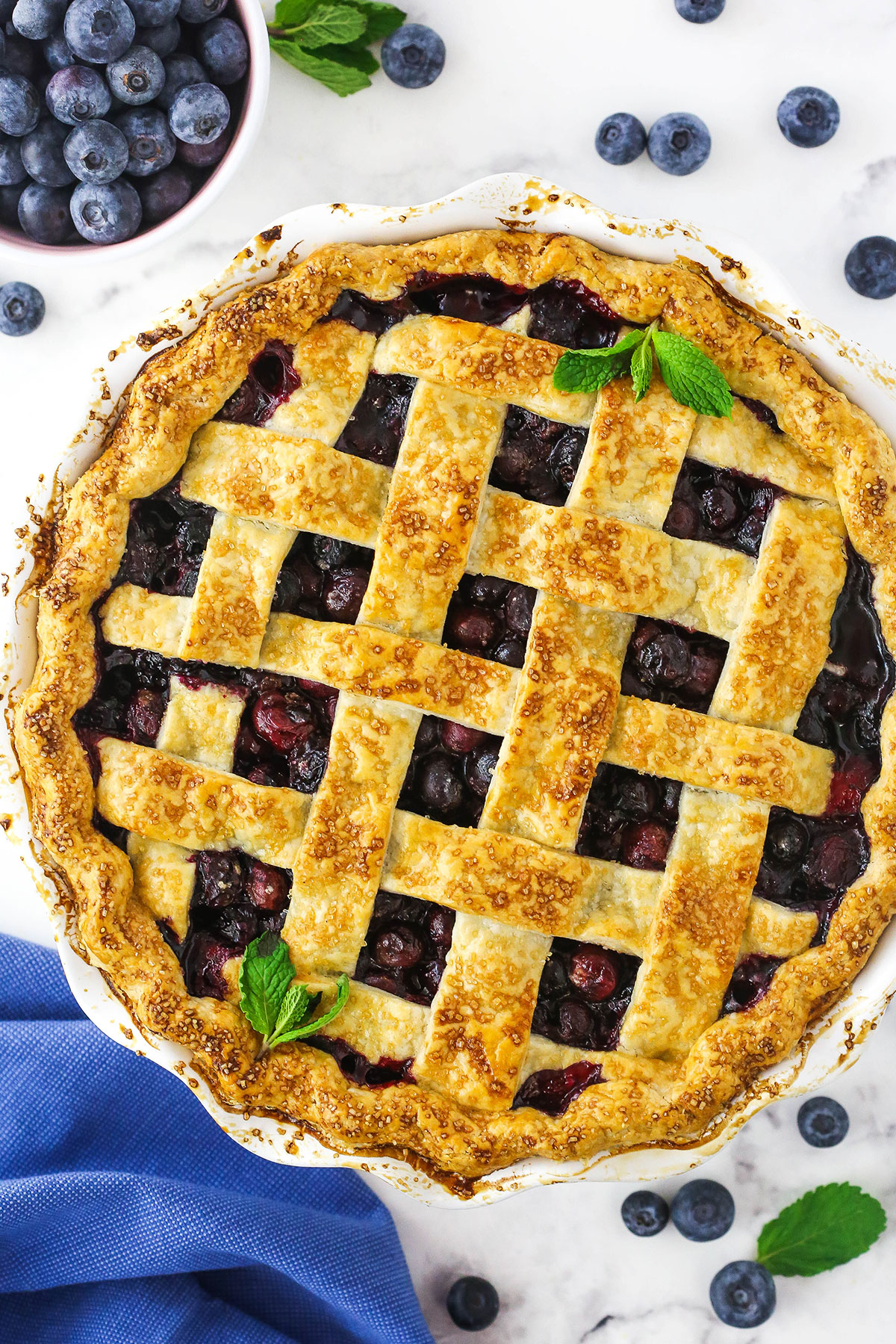 A blueberry pie on a kitchen countertop with a few fresh mint leaves on top as a garnish