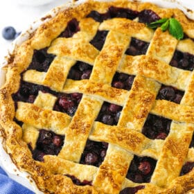 A close-up shot of a blueberry pie with a bowl of fresh berries behind it