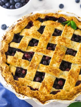 A close-up shot of a blueberry pie with a bowl of fresh berries behind it