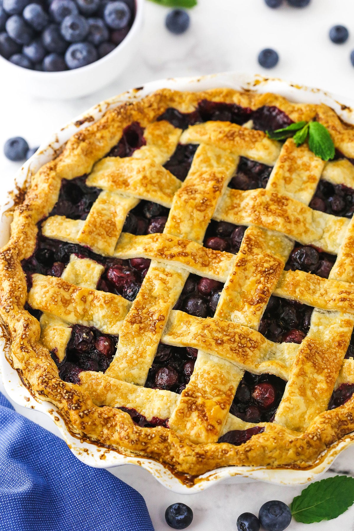 A close-up shot of a blueberry pie with a bowl of fresh berries behind it