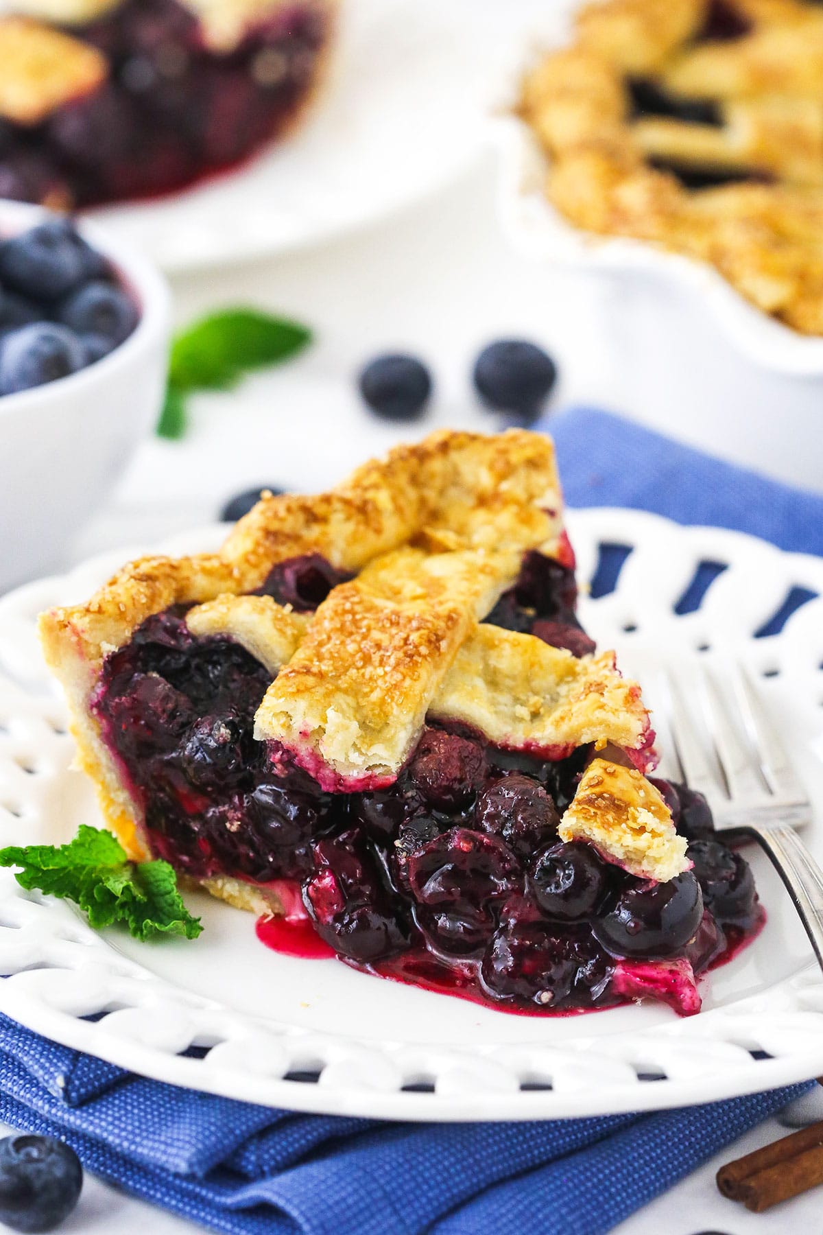 A slice of blueberry pie on a plate with a mint leaf and a fork