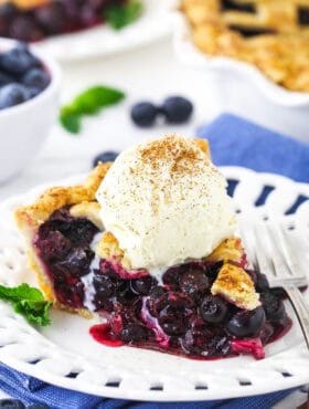 A piece of blueberry pie with a scoop of vanilla ice cream and a sprinkle of cinnamon on top