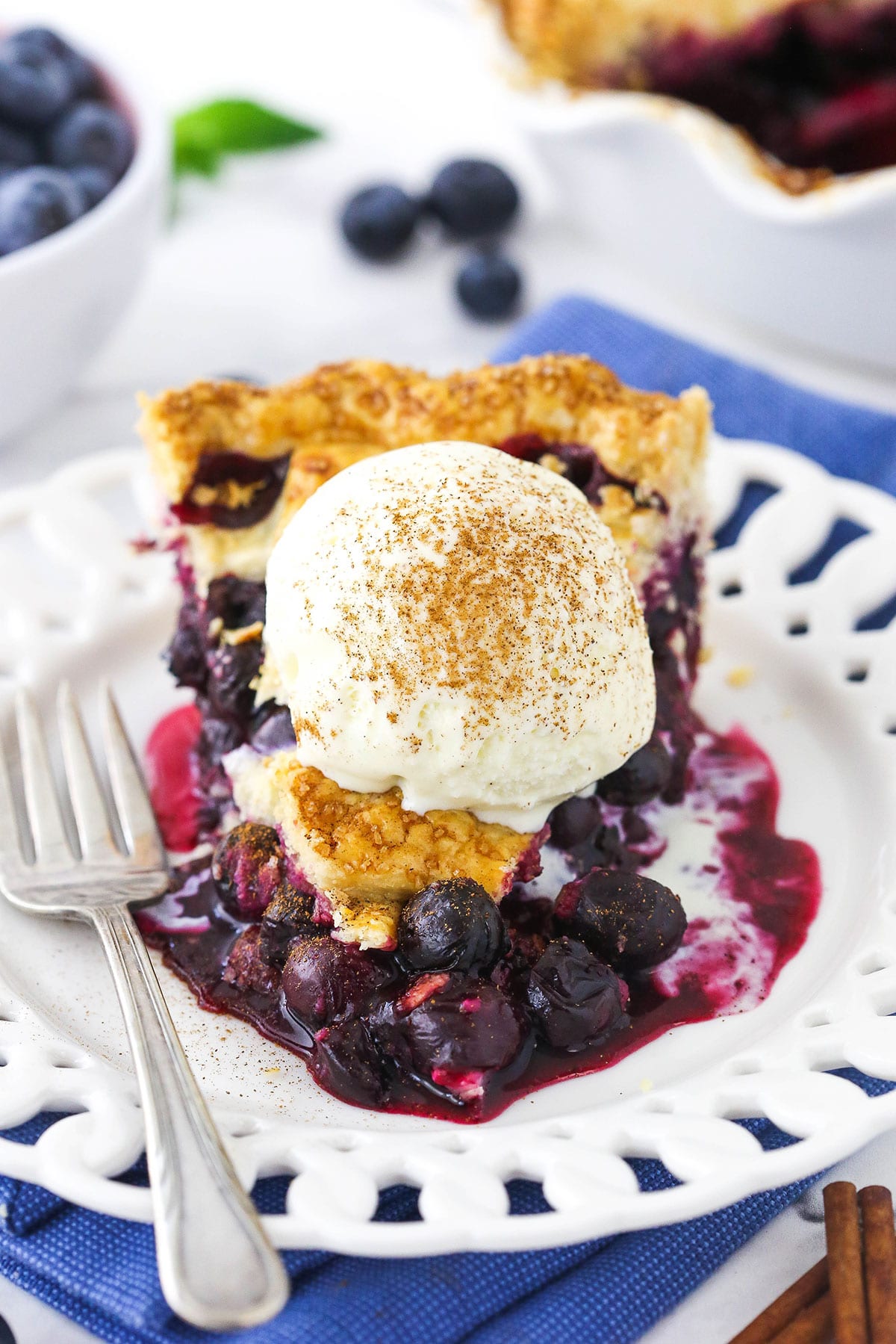 A slice of homemade blueberry pie topped with vanilla ice cream and ground cinnamon