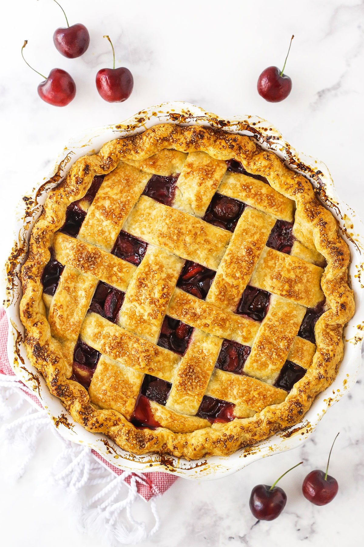 A homemade cherry pie on a marble countertop with six fresh cherries surrounding it
