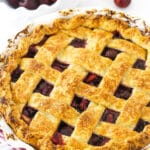 A cherry pie inside of a 9-inch pie dish with a bowl of sweet cherries in the background